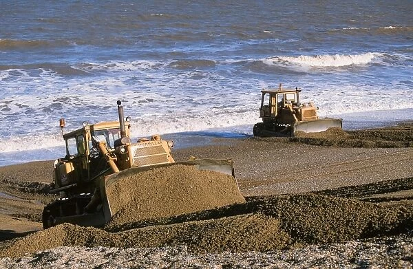 Bulldozers rebuilding the sotrm beach in Cley Norfolk UK. As climate change induced sea level rise takes hold areas of coast are increasingly at risk of