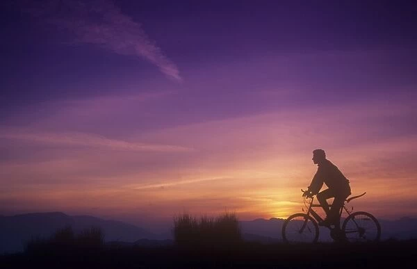 A man mountain biking at sunset on the Lake District hills, Cumbria, UK