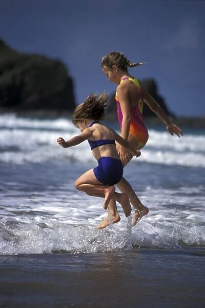 Two young girls jumping over waves, Marloes Sands, Pembrokeshire, Wales, UK, Europe