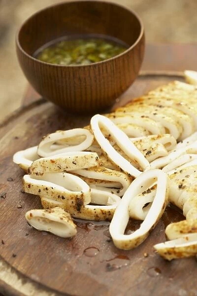 Brick-grilled squid on a wooden board, and bowl containing olive oil and coriander dressing