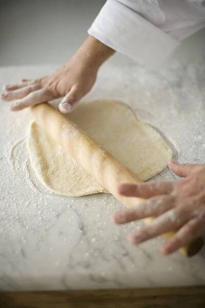 Hand rolling out pizza dough with rolling pin, close-up