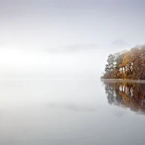 Derwent Water - autumn colours reflected in water of derwent island in the mist with catsbells just visable through the mist - Lake District - England