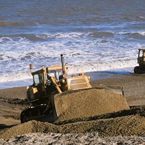 Bulldozers rebuilding the sotrm beach in Cley Norfolk UK. As climate change induced sea level rise takes hold areas of coast are increasingly at risk of