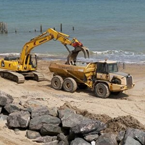 Excavator and truck on beach, repairing sea defences with boulders, Happisburgh, Norfolk, England, august