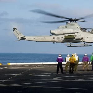 Sailors and Marines watch an AH-1Z Viper attack helicopter lift off the flight deck