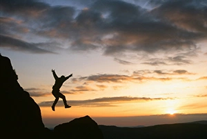 A climber jumping down a crag on Harter Fell in the Lake district Uk at sunset A climber jumping down a crag on Harter Fell in the Lake district Uk at sunset